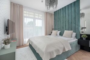 A modern bedroom with a large bed, a TV, and a nightstand with a plant.