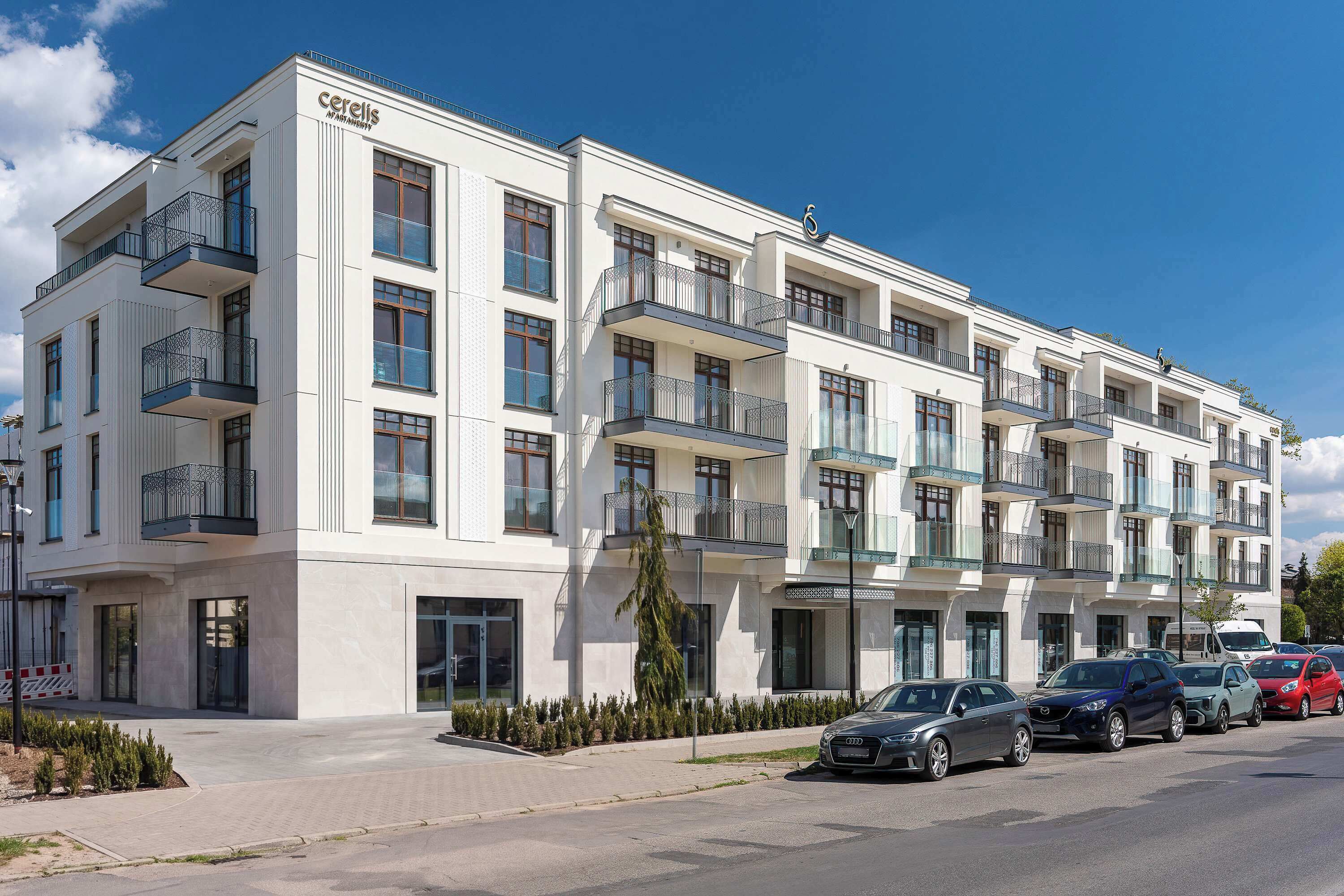 Un edificio residencial de varios pisos con balcones, un área de estacionamiento con coches y un cielo despejado.