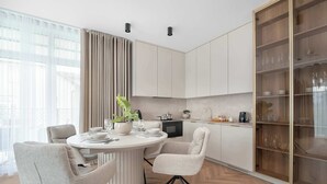 A modern kitchen with a round dining table, chairs, and a built-in cabinet with glass doors. - Stylish Apartments with Balconies | Panoramic Terrace | Close to the Brine Graduation Towers (Ciechocinek)