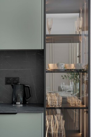 A modern kitchen with a black marble countertop, a coffee maker, and a glass display cabinet with glassware. - Stylish Apartments with Balconies | Panoramic Terrace | Close to the Brine Graduation Towers (Ciechocinek)