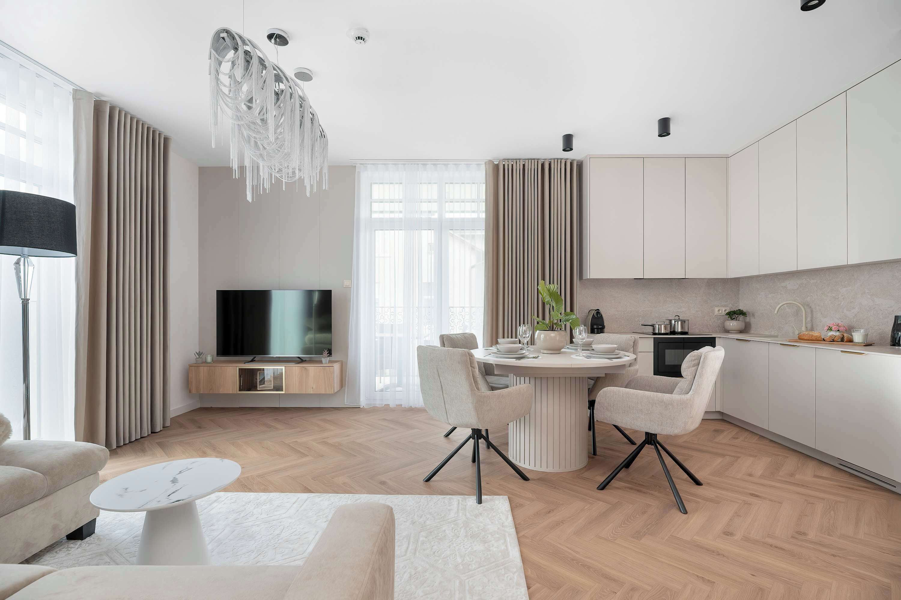 A modern kitchen with a dining area, a flat-screen TV, and a chandelier.