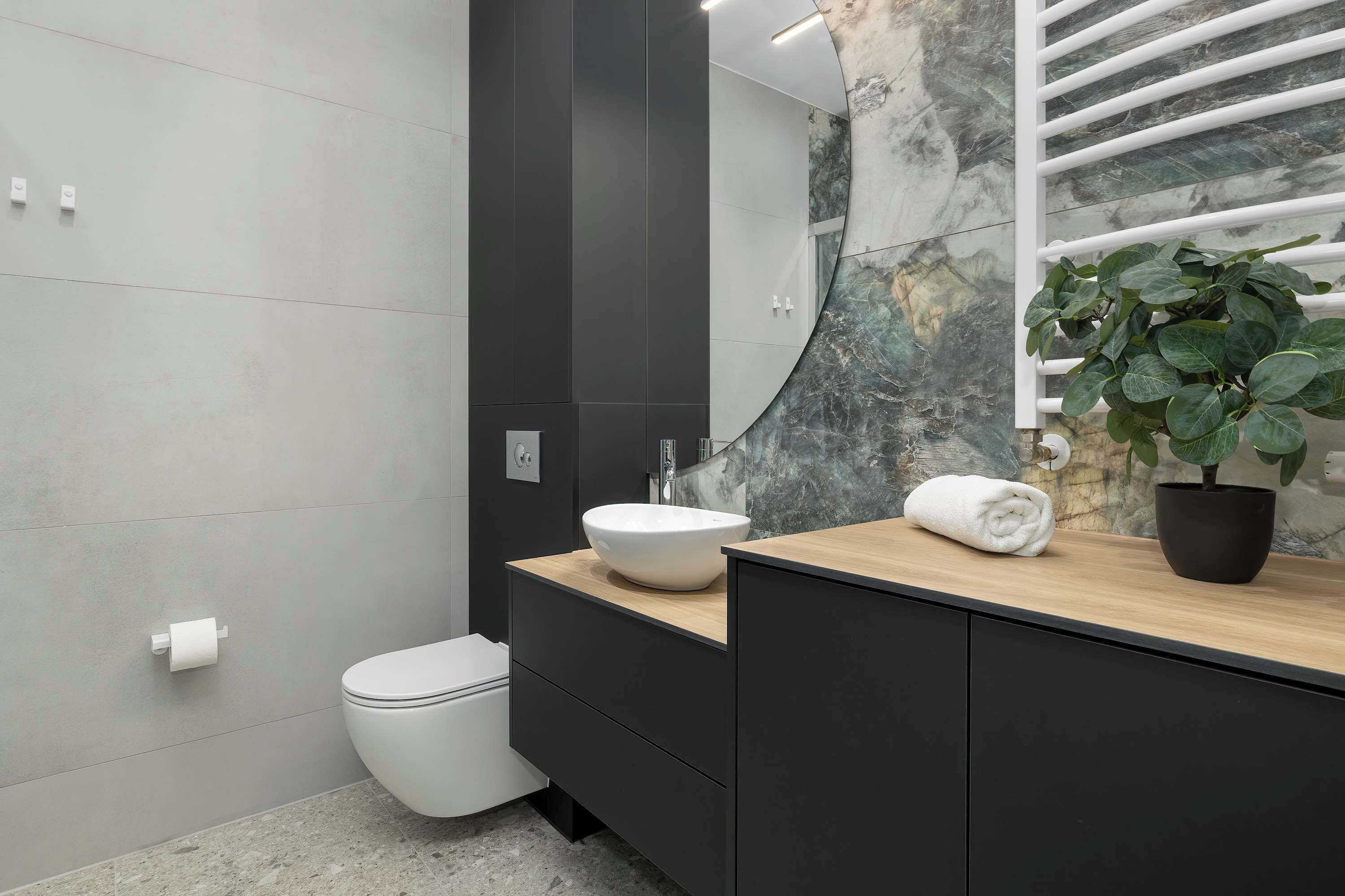 Une salle de bain moderne avec des toilettes blanches, un lavabo sur colonne, un meuble-lavabo en bois, un grand miroir et une plante en pot.