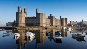 Un castillo histórico con un foso y barcos, reflejados en aguas tranquilas.