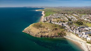 Vista aérea de un pueblo costero con playa, casas y un notable promontorio rocoso.