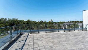 Una terrazza sul tetto con ringhiera in vetro, pavimento piastrellato e vista su un quartiere residenziale.