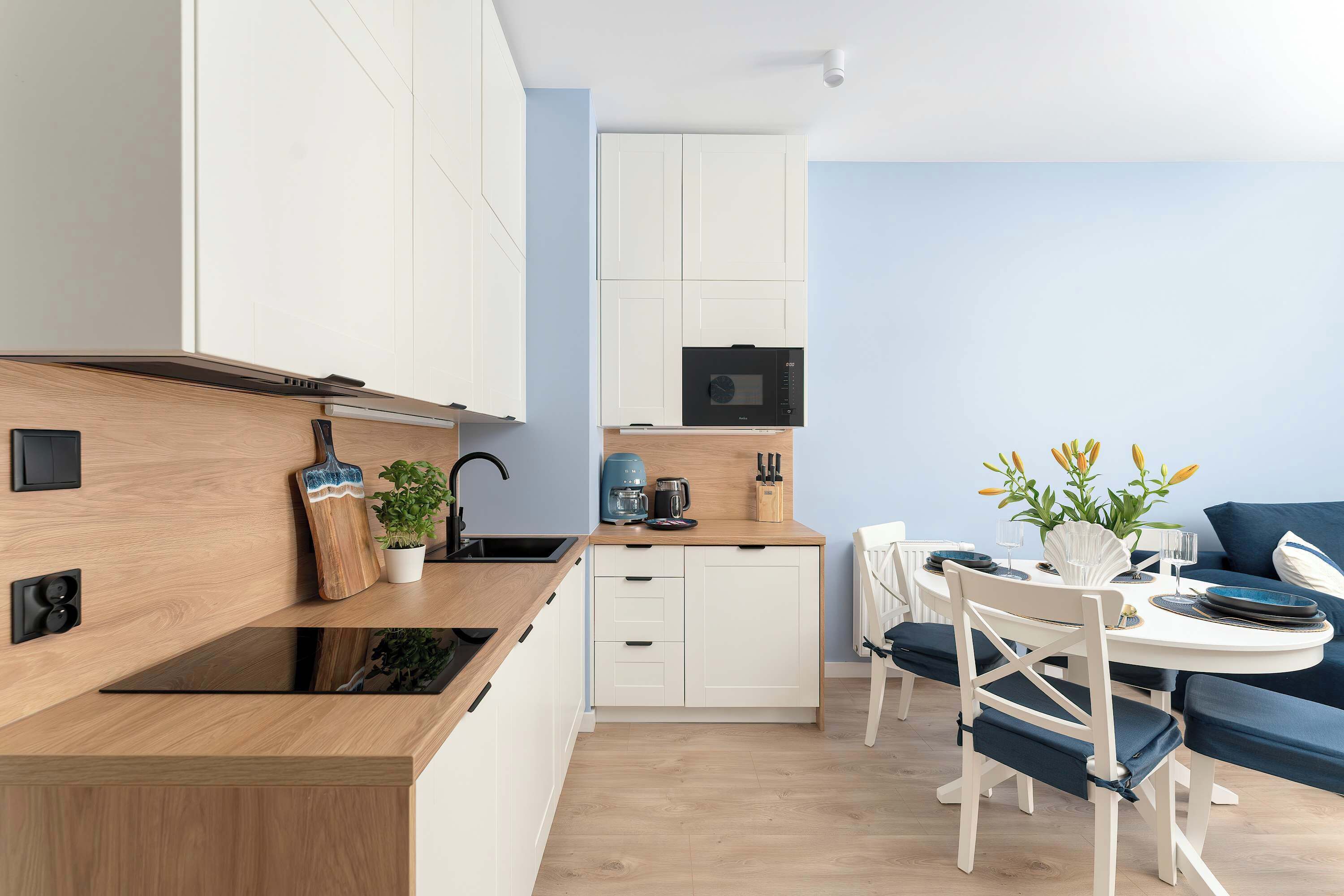 Eine moderne Küche mit weißen Schränken, einer Holz Arbeitsplatte und einem Essbereich mit blauem Sofa und weißen Stühlen.