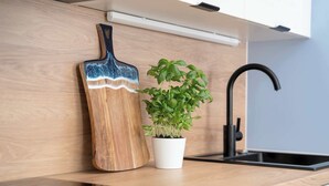 Un piano di lavoro in cucina con un tagliere di legno, una pianta di basilico in vaso e un rubinetto nero.