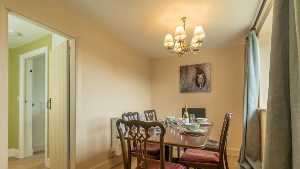Una sala da pranzo con tavolo in legno, sedie, un lampadario e un quadro appeso al muro.