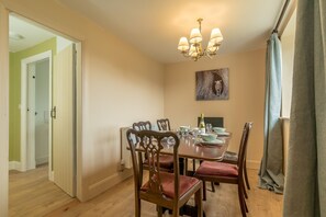 A dining room with a wooden table, chairs, a chandelier, and a painting on the wall. - Gorgeous Stone Cottage At the Foot Of The Berwyn Mountains | Ceseilgwm (Corwen)