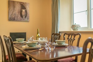 Une table à manger dressée avec des assiettes, des bols et des verres à vin, entourée de chaises en bois.