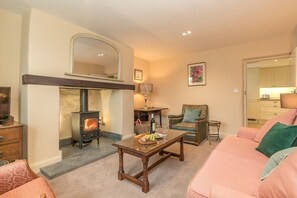 A cozy living room with a fireplace, a sofa, a chair, and a table with a bottle and glasses. - Gorgeous Stone Cottage At the Foot Of The Berwyn Mountains | Ceseilgwm (Corwen)
