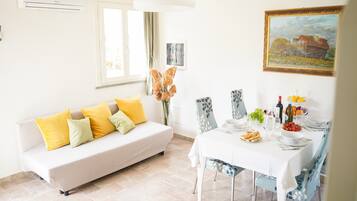 A modern living room with a sofa, dining table, chairs, and a painting on the wall.
