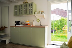 A kitchen with green cabinets, a coffee machine, and a fruit bowl.
