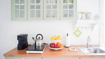 Una cucina con una macchina da caffè, un bollitore, una ciotola di frutta e un lavandino.