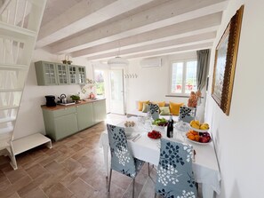 Zona pranzo con tavolo imbandito per quattro, cucina con mobili verdi e finestra con tende.