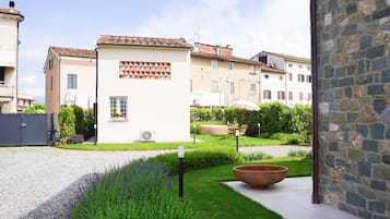 Une cour avec un bâtiment blanc, un grand mur de pierre et un chemin de gravier.
