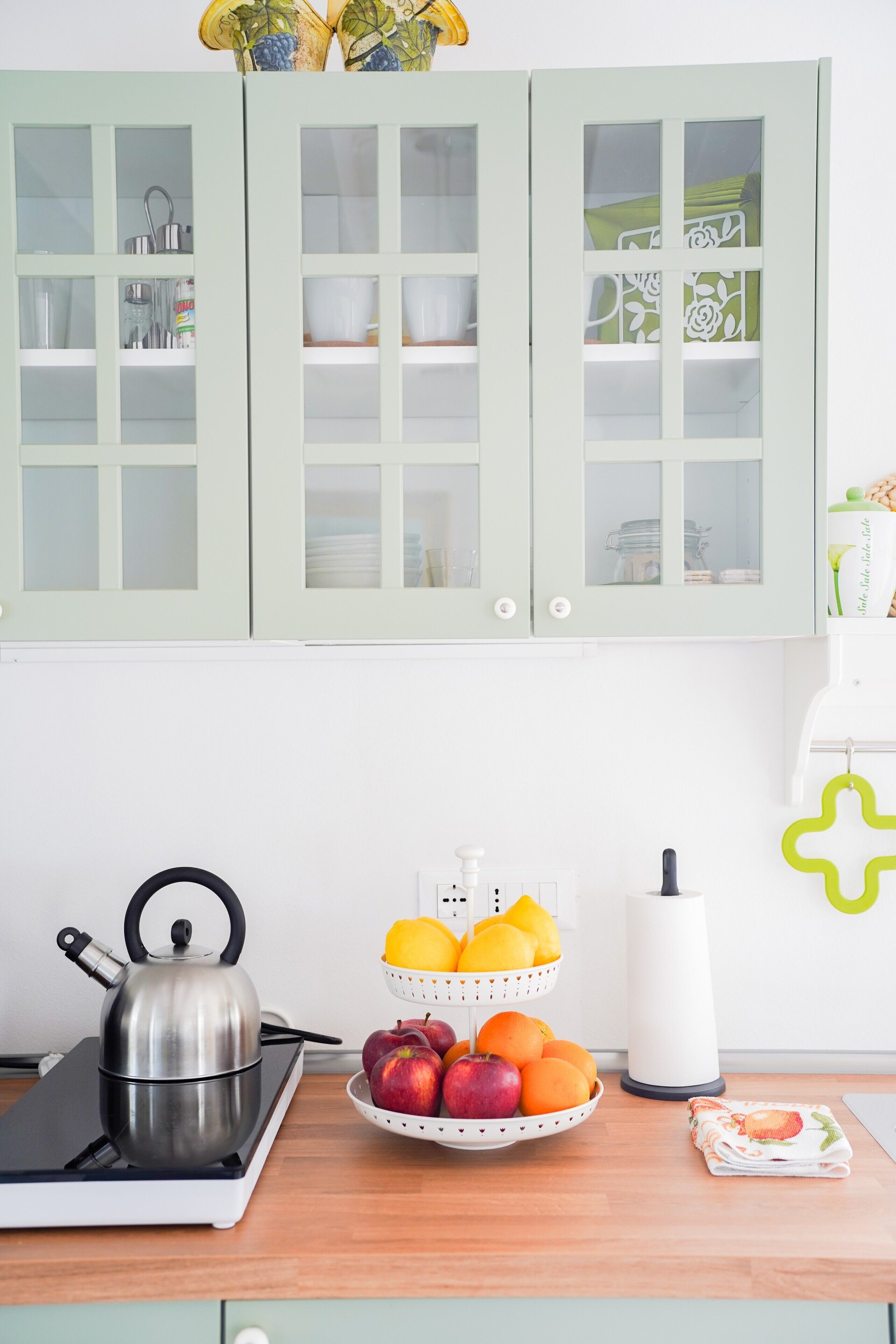 Una cucina con bollitore, una ciotola di frutta e un elettrodomestico bianco sul piano di lavoro.