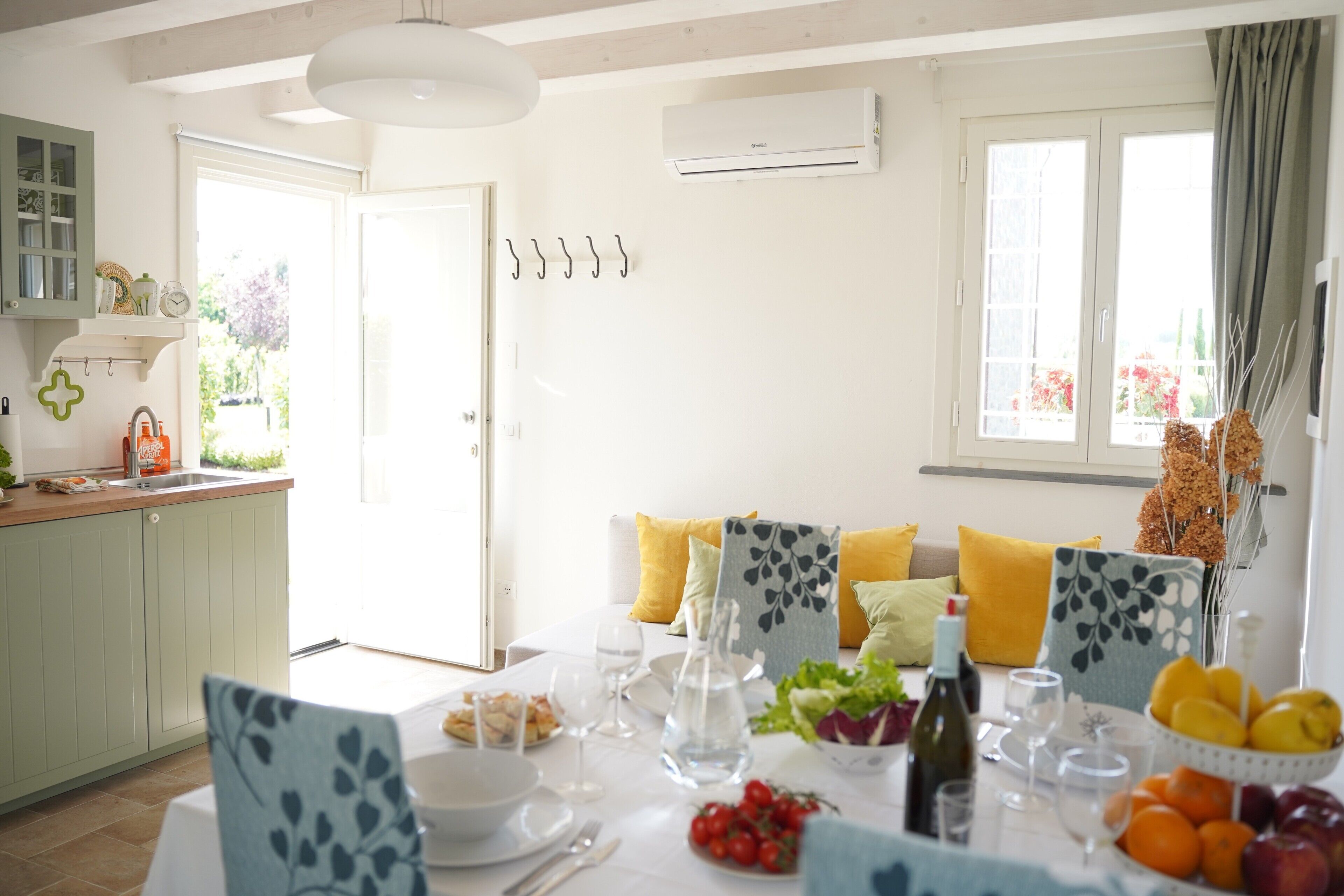 A dining area with a table set for two, a kitchen with a green cabinet, and a window with curtains.