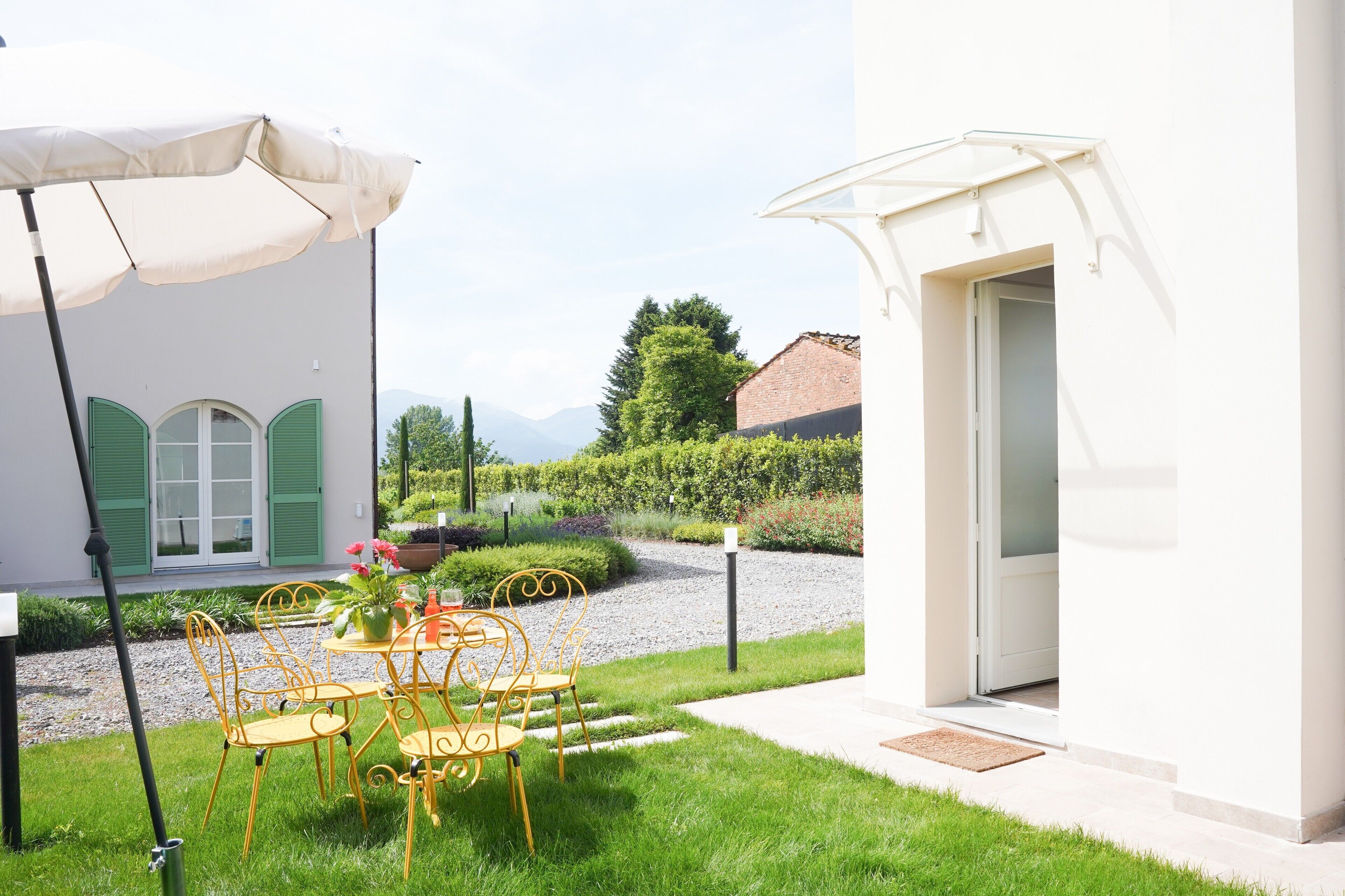 Un cortile con tavolo e sedie, una zona relax coperta e l'ingresso di un edificio.