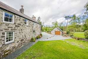 A stone house with a gravel driveway leading to a wooden door. - Cosy Cottage Near Beach with Games Room | Bwthyn-Bryn-Hir (Criccieth)