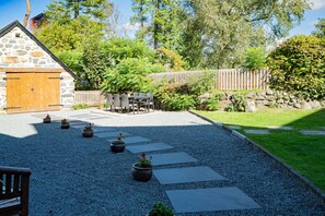 A stone building with a wooden door, outdoor seating, and potted plants. - Cosy Cottage Near Beach with Games Room | Bwthyn-Bryn-Hir (Criccieth)