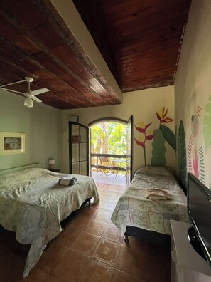 Una habitación con dos camas, ventilador de techo, televisión y vistas al exterior.