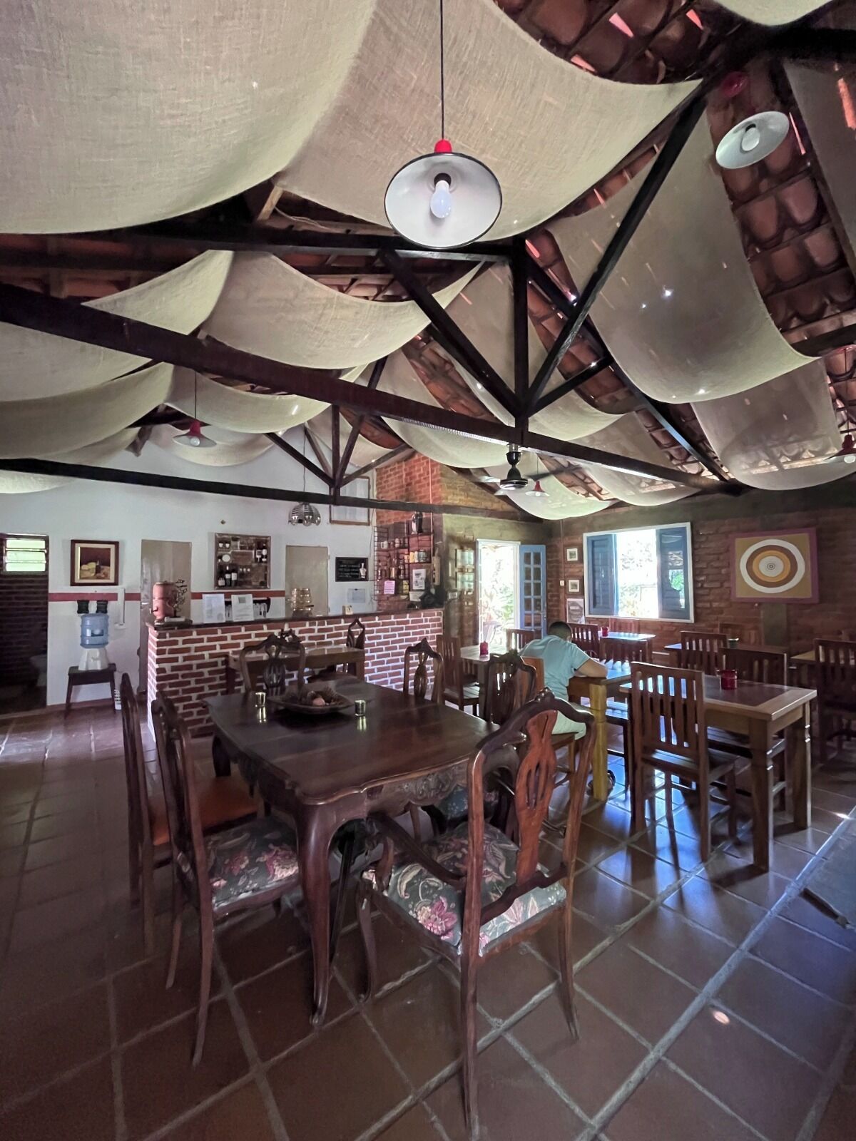 A spacious dining area with a high ceiling and exposed beams, featuring a central wooden table surrounded by chairs.