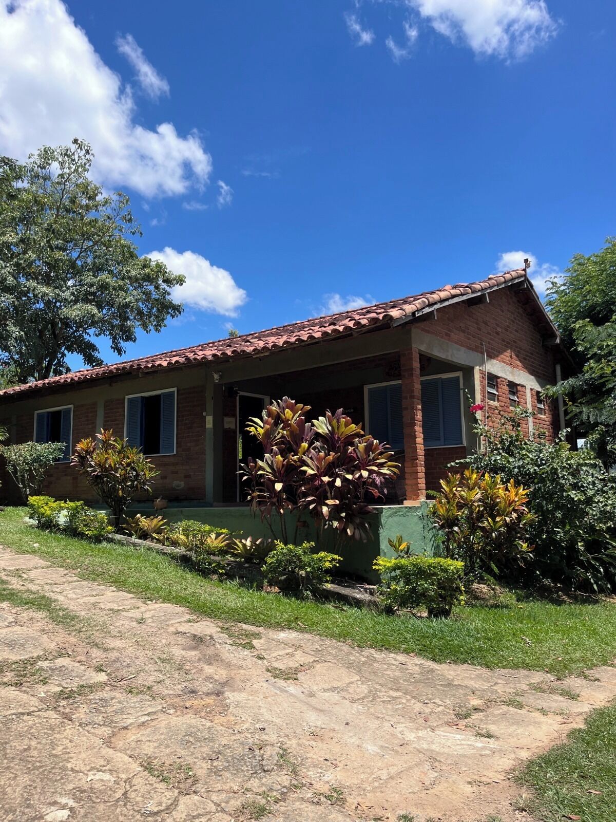 A two-story brick house with a tiled roof, a covered porch, and a well-maintained garden with various plants.