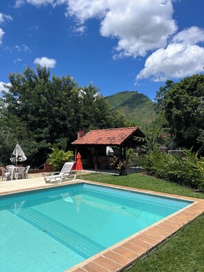 A swimming pool with a tiled edge, surrounded by a grassy area and a brick structure. - POUSADA DAS ESTRELAS (Tres Rios)