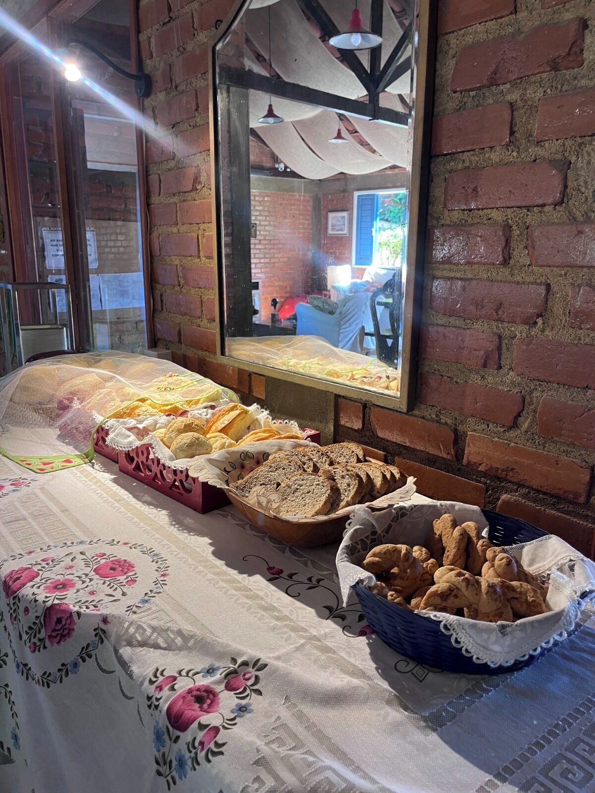 Ein reichhaltiges Buffet mit Brot und Gebäck, ein Spiegel, der den Raum widerspiegelt, und eine Backsteinwand.