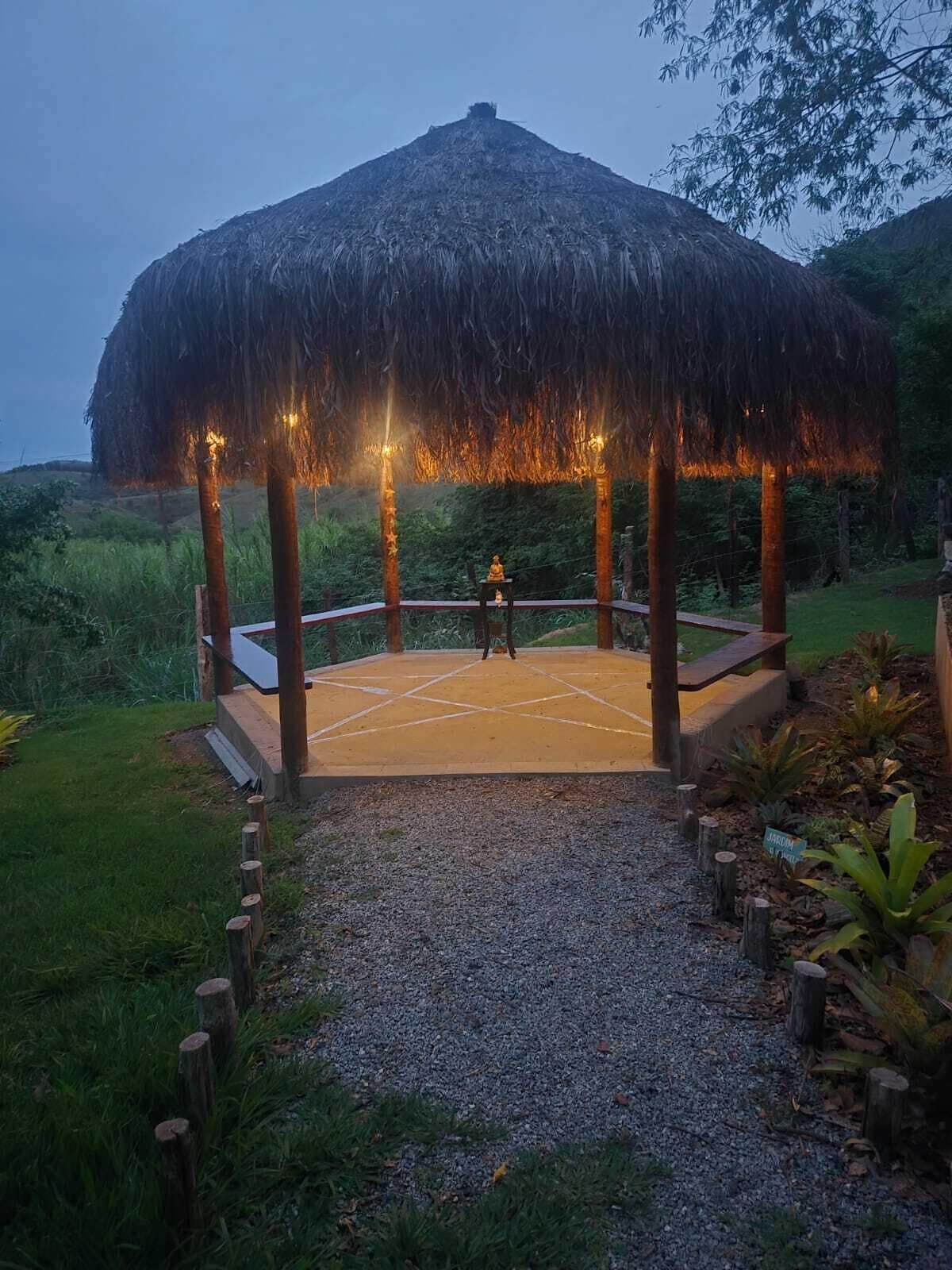 A gazebo with a thatched roof, surrounded by a gravel path and greenery.
