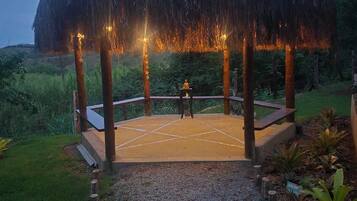 A gazebo with a thatched roof, surrounded by a gravel path and greenery.