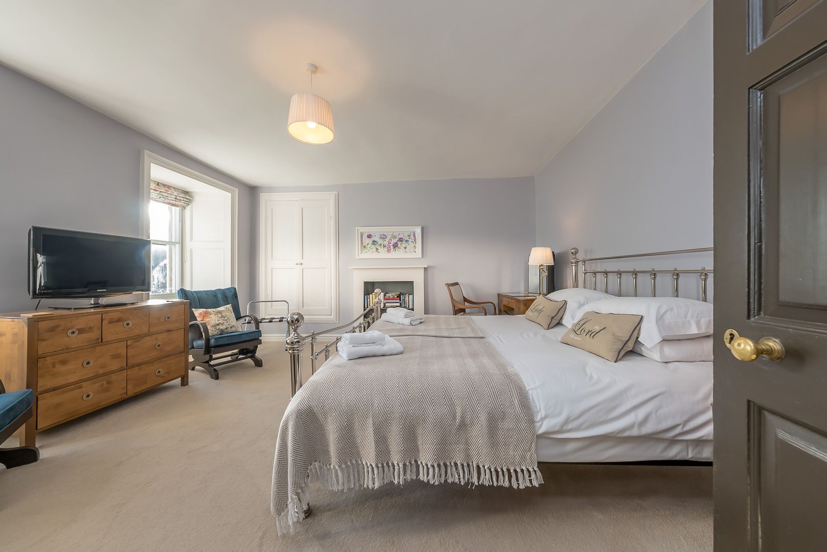 Une chambre à coucher avec un lit, une commode, un téléviseur, une chaise et une cheminée.