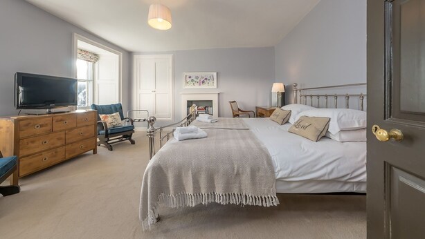 A bedroom with a bed, a dresser, a television, a chair, and a fireplace. - Georgian Country House and Stable Sleeping 18 | Gorwel-Bryn-Hir (Criccieth)