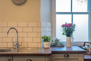 A kitchen with a sink, a potted plant, a teapot, and a vase with flowers. - Georgian Country House and Stable Sleeping 18 | Gorwel-Bryn-Hir (Criccieth)