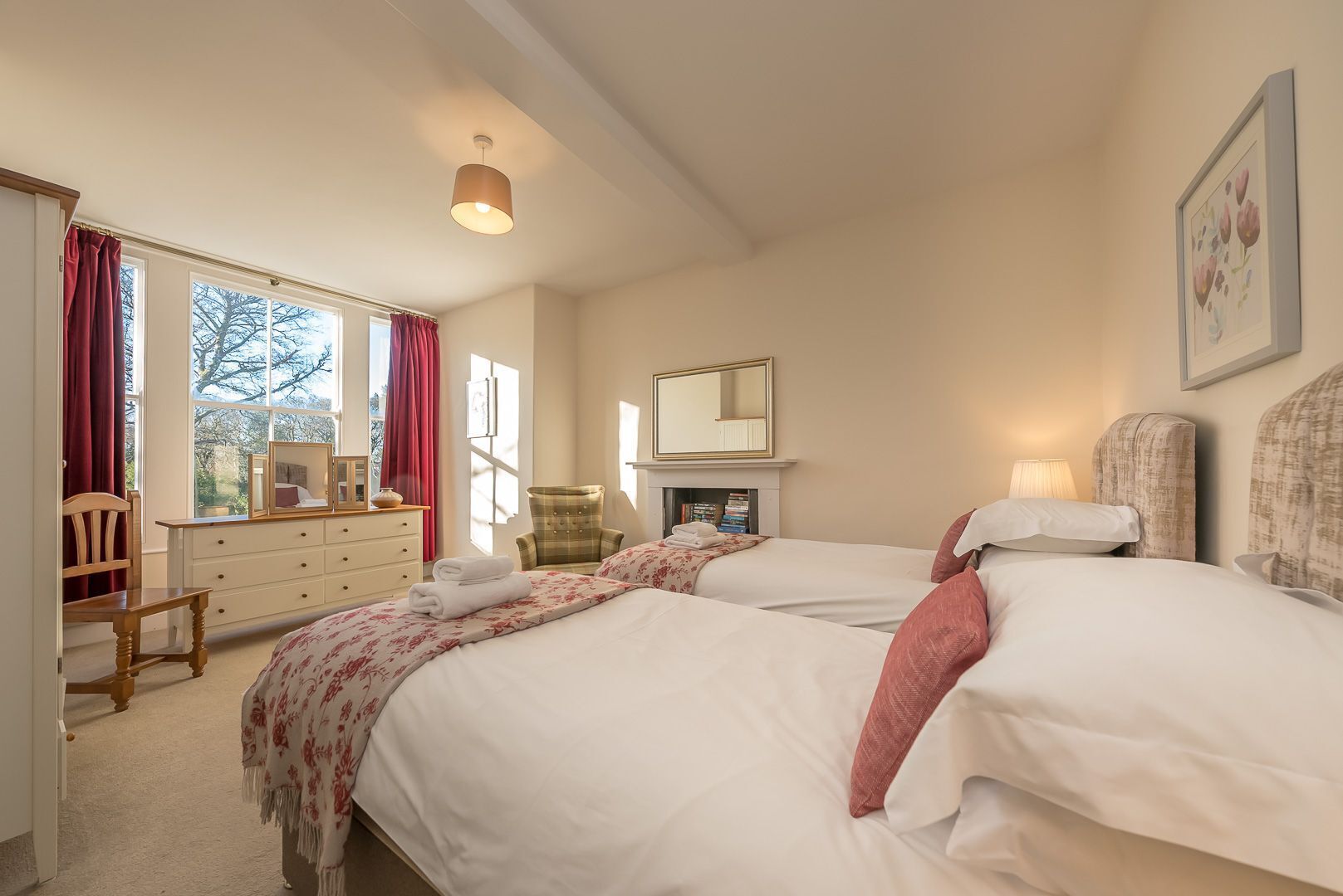 Une chambre d’hôtel avec deux lits, une commode, une chaise, une cheminée et une fenêtre avec des rideaux.