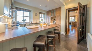 A modern kitchen with a central island, bar stools, and a view into the dining area. - Georgian Country House and Stable Sleeping 18 | Gorwel-Bryn-Hir (Criccieth)