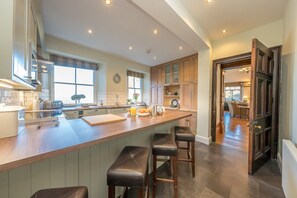 A modern kitchen with a central island, bar stools, and a view into the dining area. - Georgian Country House and Stable Sleeping 18 | Gorwel-Bryn-Hir (Criccieth)