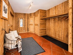 Ein Zimmer mit Holzwänden, einem Bett mit gemustertem Überwurf, einem kleinen Fenster und einem Kleiderständer.