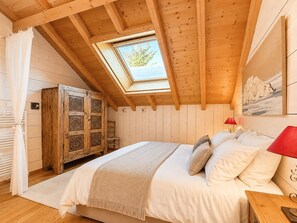 Ein Schlafzimmer mit geneigter Decke, einem Oberlicht, einem Bett mit Kissen, einem Holzschrank und einem Gemälde an der Wand.