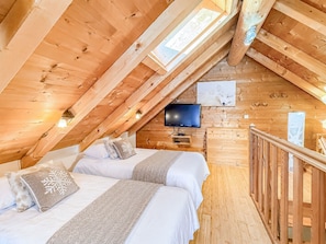 Ein gemütliches Schlafzimmer im Dachgeschoss mit zwei Betten, einem Fernseher und Holzwänden.
