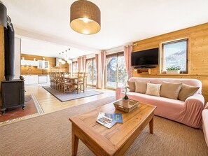 A cozy living room with a wooden coffee table, a pink sofa, and a television mounted on the wall. - Chalet Mahana - Valloire - Sleeps 12 with Panoramic Mountain Views (Valmeinier)