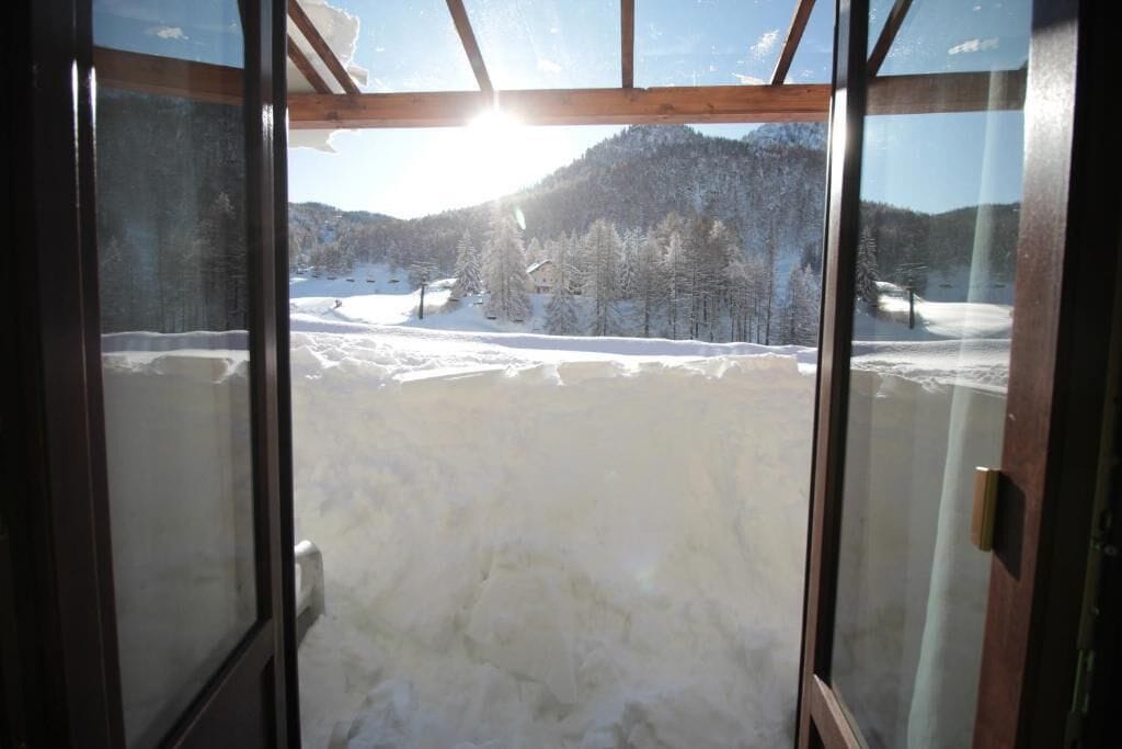 A room with a large window overlooking a snowy landscape with trees and mountains.