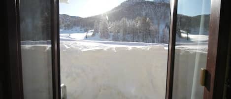 A room with a large window overlooking a snowy landscape with trees and mountains.