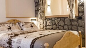 A bed with a patterned bedspread, a headboard, and curtains tied back. - Hotel Al Foiron (Claviere)
