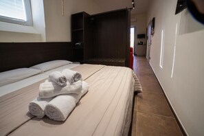 Quarto de hotel com uma cama, um guarda-roupa e uma casa de banho visível através de uma porta aberta.