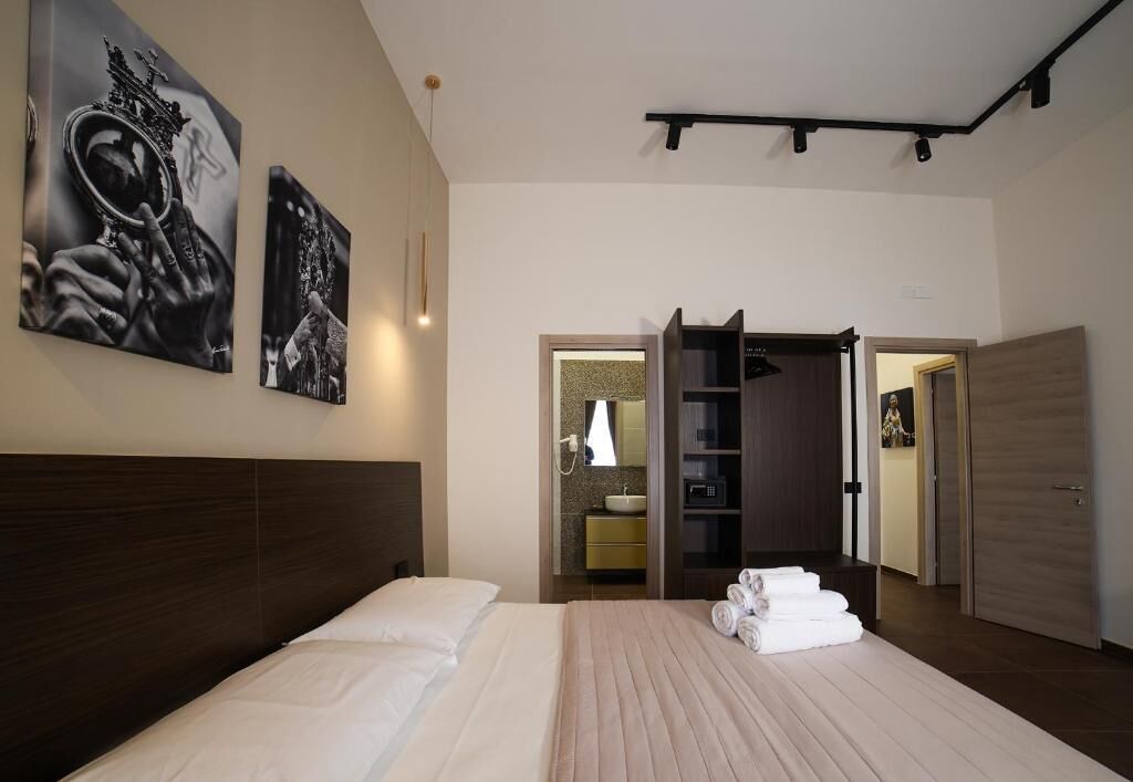 A hotel room with a large bed, a wardrobe, a bathroom with a sink and mirror, and two framed pictures on the wall.