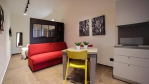 A compact living space with a red sofa, a yellow chair, a small table with potted plants, and a kitchenette area. - Sciuscià beb spaccanapoli (Naples)