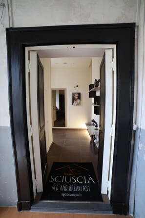 A hotel entrance with a black mat reading 'SCIUSCIA BED AND BREAKFAST Spaccanapoli' leading to a hallway with a painting and a sink. - Sciuscià beb spaccanapoli (Naples)
