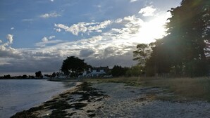 Una spiaggia con una casa sullo sfondo, cielo sereno e luce solare.